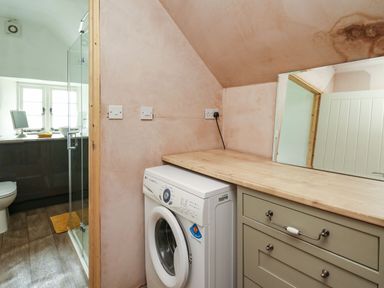 A laundry area with a washing machine under a wooden countertop and a mirror next to a bathroom with a glass shower door at The Bake House in Bettws