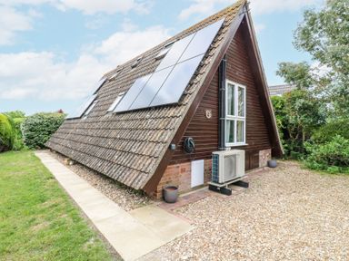 An A-frame house with solar panels on the roof a paved walkway grassy area and gravel driveway at Kingfisher in Isleham