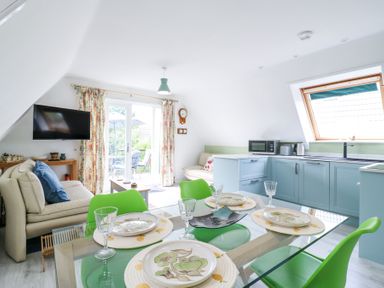 A kitchen and dining area with blue cabinets green chairs and a beige sofa at Kingfisher in Isleham