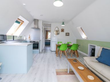 An open plan kitchen and dining area with light blue cabinets green dining chairs and a beige sofa at Kingfisher in Isleham