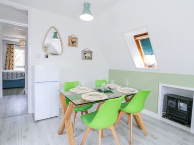 A dining room with a glass table and green chairs near a refrigerator and a small stove at Kingfisher in Isleham