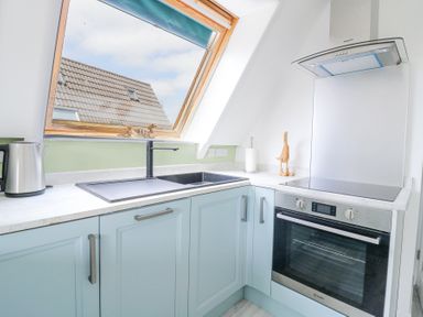 A kitchen corner with a sink under a slanted window a kettle and an oven at Kingfisher in Isleham