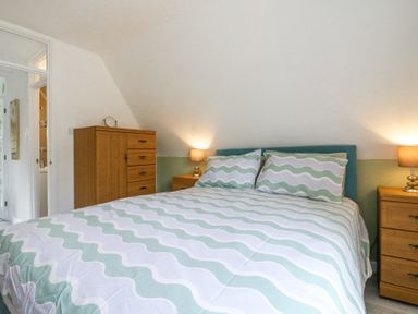 A bedroom with a bed with wavy patterned bedding two bedside tables with lamps and a wooden chest of drawers at Kingfisher in Isleham