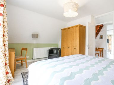 A bedroom with a wooden wardrobe a black armchair a wooden chair and desk patterned curtains and a bed with a patterned bedspread at Kingfisher in Isleham