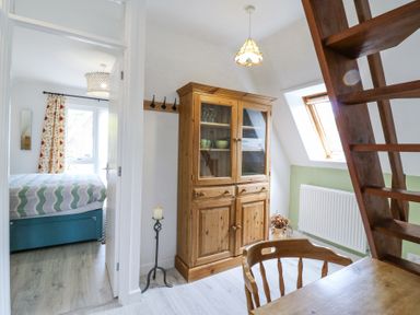 A room with a wooden cabinet a wooden chair and table and an open door to a bedroom at Kingfisher Isleham