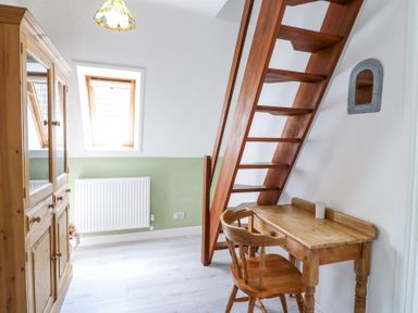 A small room with wooden stairs a wooden desk and chair a wooden wardrobe and a window at Kingfisher in Isleham