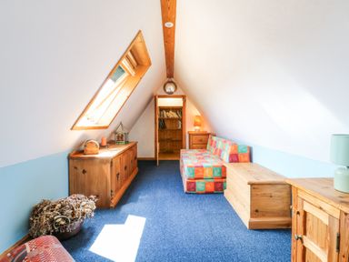 An attic room with a skylight window a wooden cabinet a colorful sofa a wooden chest and a bookshelf at Kingfisher in Isleham