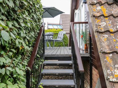 An outdoor staircase leading to a small patio with striped chairs and an umbrella near a house with a tiled roof at Kingfisher in Isleham