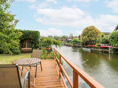 A wooden deck with table and chairs overlooking a canal with boats and houses at Kingfisher Isleham