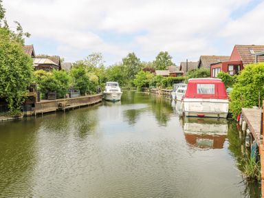 A canal with boats docked along both sides and houses with gardens along the banks at Kingfisher in Isleham