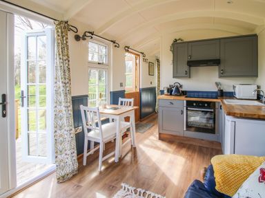 A kitchen area with grey cabinets white dining table and chairs wooden countertops and open doors to outside at Mucklewick Hollow in Minsterley near Bishops Castle