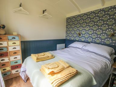 A bedroom with a double bed with white bedding and yellow towels on a green blanket at Mucklewick Hollow in Minsterley near Bishops Castle