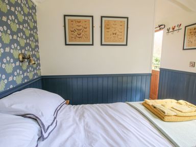 A bedroom with a bed with white sheets and folded towels on it blue paneling and butterfly framed prints on the wall at Mucklewick Hollow Minsterley near Bishops Castle