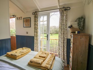 A bedroom with folded towels on a bed and glass doors leading to a garden at Mucklewick Hollow in Minsterley near Bishops Castle