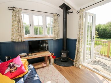 A living room with a blue sofa a wooden TV stand a black wood stove and open glass doors leading to a patio at Mucklewick Hollow in Minsterley near Bishops Castle