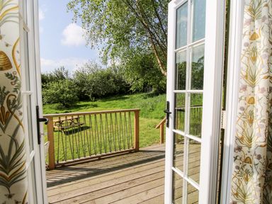 A wooden deck with railing looking out to a grassy backyard with trees and a picnic table at Mucklewick Hollow in Minsterley near Bishops Castle