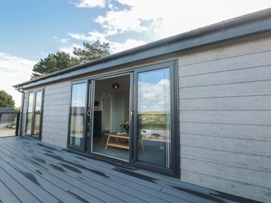 Sliding glass doors open to a living room with a wooden coffee table on a deck outside at Bluebell Lodge in Norton near Dartmouth