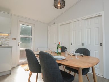 A dining area with a wooden table set with plates glasses and bottles and four dark upholstered chairs at Bluebell Lodge in Norton near Dartmouth