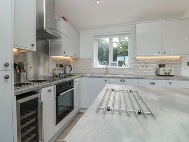 A modern kitchen with white cabinets a gas stove an oven a wine cooler and a window at Bluebell Lodge in Norton near Dartmouth