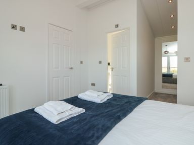A bedroom with a bed with folded towels on a blue blanket two white doors and a full-length mirror at Bluebell Lodge in Norton near Dartmouth
