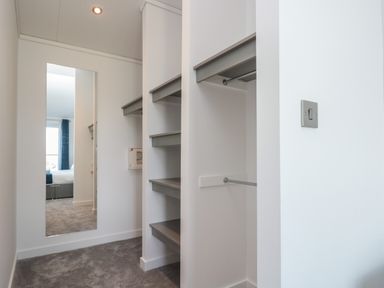 A walk-in closet with shelves a hanging rod and a mirror reflecting a bedroom at Bluebell Lodge in Norton near Dartmouth