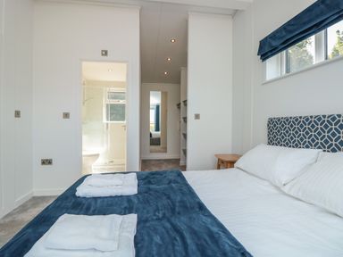 A bedroom with a bed towels and a window next to a bathroom and hallway at Bluebell Lodge in Norton near Dartmouth