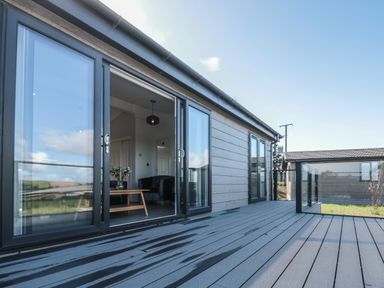 A deck area outside a house with glass doors leading to a living room at Bluebell Lodge in Norton near Dartmouth
