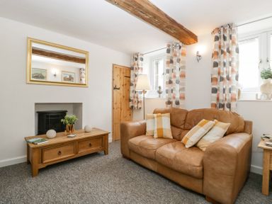 A living room with a brown leather sofa a wooden coffee table a floor lamp patterned curtains and a wall mirror at 4 Wallflower Row in Mordiford near Hereford