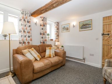 A sitting room with a brown leather sofa patterned curtains and wooden door at 4 Wallflower Row Mordiford near Hereford