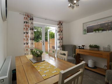 A dining room with wooden table and white chairs next to glass doors with patterned curtains at 4 Wallflower Row Mordiford near Hereford