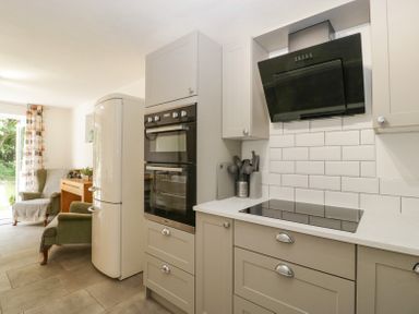 A kitchen with built-in double oven stovetop and refrigerator next to a sitting area with armchairs at 4 Wallflower Row Mordiford near Hereford