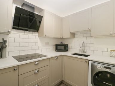 A kitchen with beige cabinets a black stovetop a black microwave a stainless steel sink and a washing machine at 4 Wallflower Row Mordiford near Hereford