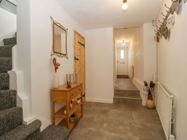 A hallway with stairs carpeted in gray on the left a wooden console table with decorative items a mirror above a wooden door and a white front door at the end at 4 Wallflower Row Mordiford near Hereford