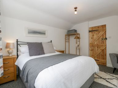 A bedroom with a bed white bedding cushions wooden nightstand lamp wooden door and clothes rack at 4 Wallflower Row Mordiford near Hereford