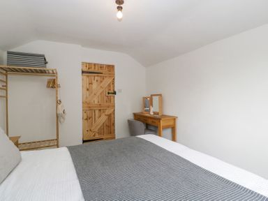 A bedroom with a bed a wooden door a wooden rack with hangers and a wooden desk with a chair at 4 Wallflower Row Mordiford near Hereford