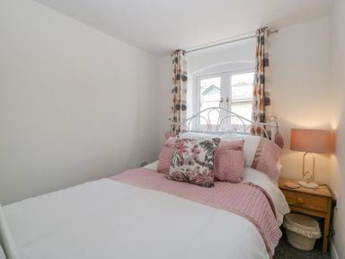A bedroom with a white metal bed frame pink bedding wooden nightstand and patterned curtains at 4 Wallflower Row in Mordiford near Hereford