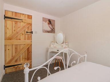A bedroom with a white metal bed frame a wooden door a white dressing table with an oval mirror and a stool at 4 Wallflower Row Mordiford near Hereford