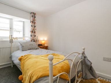 A bedroom with a single bed a yellow blanket a bedside table with a lamp and a window with patterned curtains at 4 Wallflower Row Mordiford near Hereford