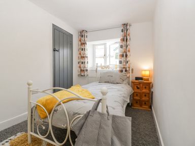 A small bedroom with a single bed a bedside table with a lamp patterned curtains and a dark door at 4 Wallflower Row Mordiford near Hereford