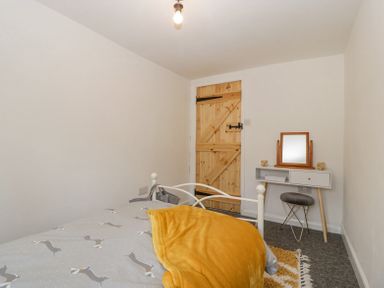 A bedroom with a bed a wooden door a vanity table with a mirror and a stool at 4 Wallflower Row Mordiford near Hereford