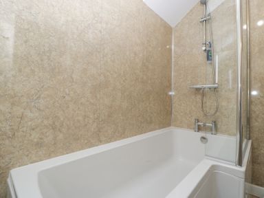 A bathtub with mounted shower head and glass shower screen in a bathroom at 4 Wallflower Row Mordiford near Hereford