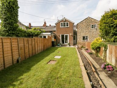 A backyard with grass lawn flower beds and a two story brick house at 4 Wallflower Row Mordiford near Hereford