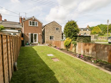 A backyard garden with grass lawn and flower beds next to a brick and stone house at 4 Wallflower Row Mordiford near Hereford