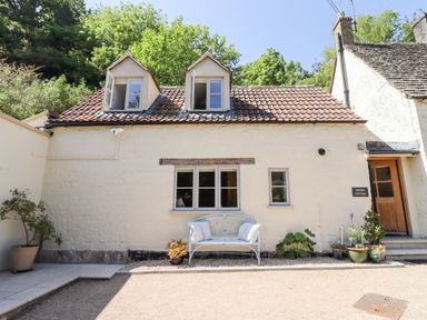 Exterior of a cottage with two dormer windows a bench and potted plants at Spring Cottage in Stroud