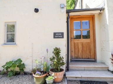 A wooden door with glass panes next to a wall with a Spring Cottage sign and potted plants at Spring Cottage in Stroud