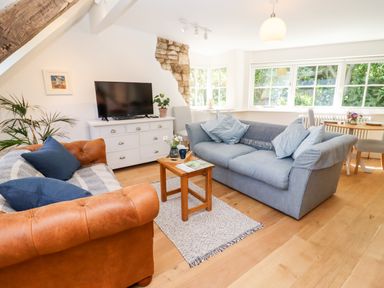 A living room with two sofas a wooden coffee table a white TV stand with a television and large windows at Spring Cottage in Stroud