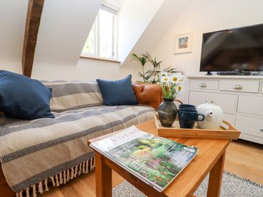 A living room with a sofa covered with a blanket and cushions and a wooden coffee table with a magazine and a tray with a teapot mugs and flowers at Spring Cottage in Stroud