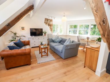 A living room with sofas a wooden coffee table a television and large windows at Spring Cottage in Stroud