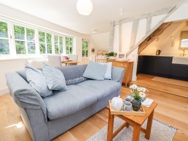 A living room with a blue sofa and small wooden table with tea set next to a kitchen area at Spring Cottage in Stroud