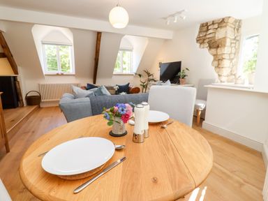 A dining table with plates and cutlery in a living room with sofas and a television at Spring Cottage in Stroud